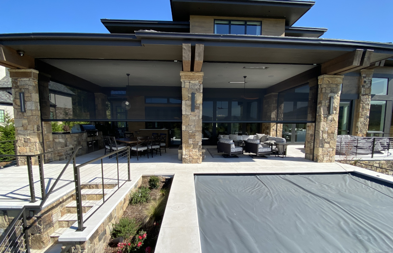 Luxury outdoor patio with retractable screens providing shade and privacy, overlooking a covered pool area.