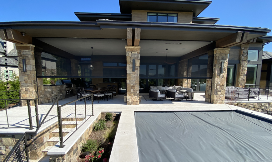 Luxury outdoor patio with retractable screens providing shade and privacy, overlooking a covered pool area.